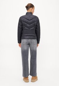 Zwarte pufferjas met chevron-stiksel, slim fit ontwerp en hoge kraag. Gecombineerd met grijze jeans met wijde pijpen en tan laarzen.