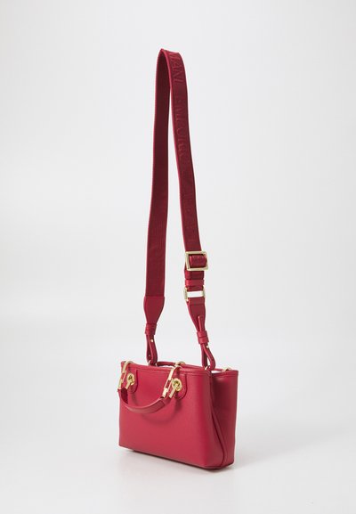 Bolso de mano rojo de cuero con herrajes dorados, doble asa superior y una correa larga regulable con un diseño de logo texturizado. Forma rectangular.