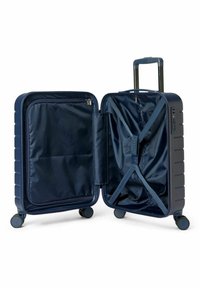 Valise rigide bleu marine avec une poche intérieure zippée et des sangles croisées pour sécuriser les objets. Elle est équipée de quatre roues et d'une poignée rétractable.