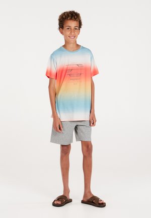 T-shirt a maniche corte con un design a gradiente nei colori blu, arancione e rosso, accompagnato da una stampa grafica nera. Abbinato a pantaloni corti grigi e sandali marroni.