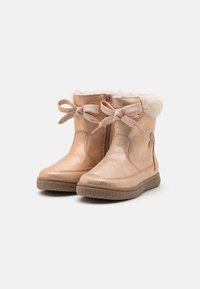 Botas tobilleras de color oro rosa con ribete de pelo sintético, cordones en la parte delantera, cremallera lateral y suela de goma texturizada. Acabado metálico suave con detalles cosidos.
