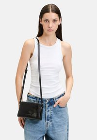 Schwarze Leder-Crossbody-Tasche mit rechteckiger Form und glatter Textur, ausgestattet mit einem langen Riemen und silbernen Hardware-Akzenten.