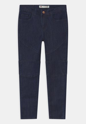 Jean slim en denim bleu foncé avec bouton frontal, passants de ceinture et coutures distinctes aux genoux et aux cuisses supérieures.