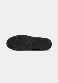 Semelle de chaussure noire avec des crampons à motifs, un dessin circulaire près du talon et le nom de la marque "Hilfiger" embossé au centre.