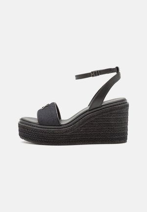 Sort kile-sandal med flettet platformsål, åben tå-rem og justerbar ankelrem med spænde.
