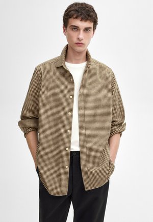 Brown and beige checkered shirt, button-up with a collar, rolled sleeves, soft cotton fabric, styled over a white t-shirt and black pants.