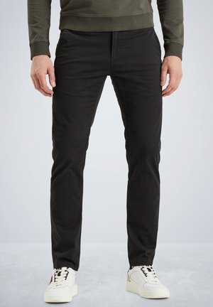 Black slim-fit pants with a smooth cotton blend fabric. Features front pockets and subtle stitching details. Worn with white sneakers.