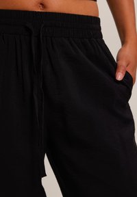 Pantalons noirs, légers, avec taille élastique et cordon de serrage. Dotés de poches latérales et d'une texture lisse. Conception décontractée.