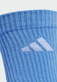 Calcetines de color azul claro, estriados y fabricados en un tejido suave, que presentan un logotipo blanco con un patrón de tres rayas en el lateral.