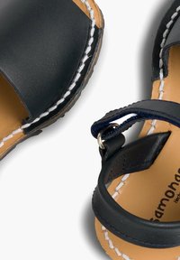 Granatowo-niebieskie skórzane sandały z okrągłym noskiem, białymi przeszyciami oraz regulowanym paskiem na kostce z metalową pętelką.