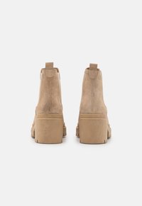 Stivali alla caviglia in suede beige con suola spessa, dotati di una linguetta sul retro e texture liscia. Nessun marchio visibile all'esterno.