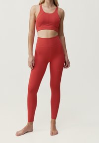 Röd sport-bh och högmidjade leggings i ett mjukt, elastiskt material. Noterbara sömdetaljer och subtila perforeringar på sidorna.