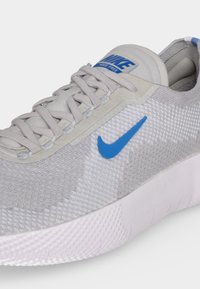Κοντινή λήψη ενός ανοιχτόγκρι Nike Free αθλητικού παπουτσιού με μπλε λογότυπο Swoosh και λευκή υφή στην σόλα.