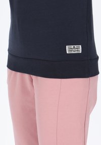Felpa blu navy con orlo a costine e un piccolo etichetta bianca; abbinata a pantaloni rosa chiaro caratterizzati da un dettaglio di cucitura visibile.