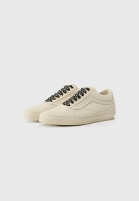 Cream-colored suede low-top sneakers with black patterned laces, rubber sole, and side detailing in a classic skate shoe design.