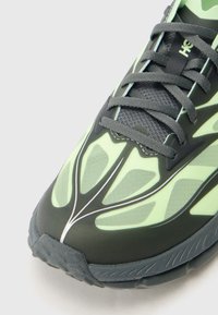 Roheline ja must spordijalats, millel on tekstureeritud võrgust pealiskest, keerukas lehemuster ja hallid paelad kummist tallaga.