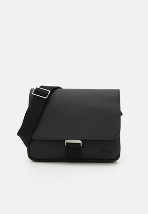 Saco mensageiro preto feito de material texturizado, com fecho de aba, alça ajustável e metais. Apresenta um detalhe de logo na parte da frente.