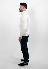 Ecru pullover met een ritskraag, aansluitend ontwerp, gecombineerd met donkerblauwe slim-fit broek en zwarte instapschoenen.