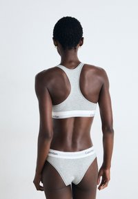 Gray cotton sports bra and matching thong with racerback design, featuring a white waistband with Calvin Klein logo. Smooth texture.