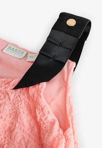 Gaiši rozā audums ar teksturētām rievām, ar melnu satīna siksnu un zelta pogu detaļām, kā arī etiķeti ar uzrakstu "BAKER by Ted Baker."