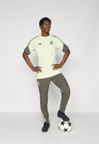 Maillot de sport vert clair avec des manches gris foncé et un logo ; pantalon gris assorti avec des accents rayés. Chaussures de foot noires et ballon inclus.