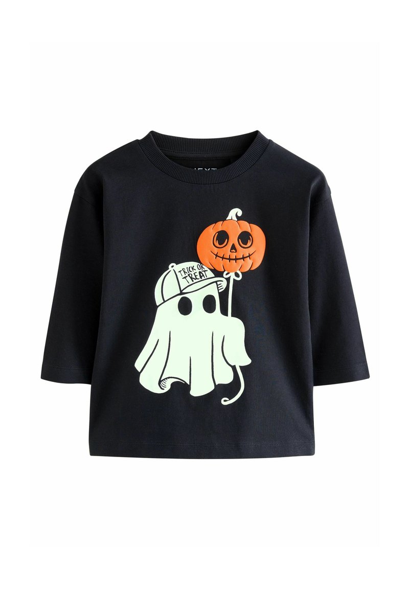 Fekete, rövid ujjú póló, fehér szellemmel, amely egy narancssárga tököt tart, a "Trick or Treat" felirattal és egy sapkával.