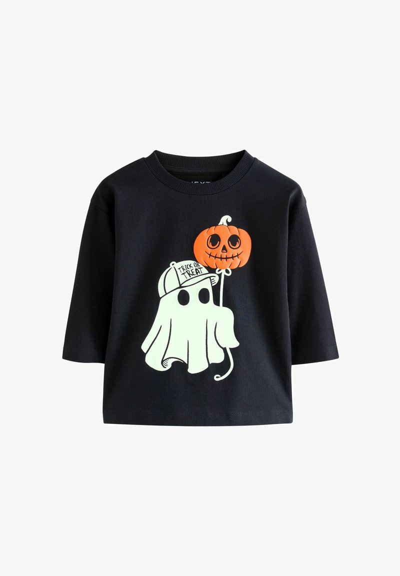 Fekete, rövid ujjú póló, fehér szellemmel, amely egy narancssárga tököt tart, a "Trick or Treat" felirattal és egy sapkával.