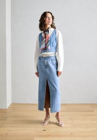 Jupe maxi en denim avec une fente avant, assortie à un top en denim court et un foulard en soie rayé coloré. Elle présente une ceinture blanche et des talons à lanières.