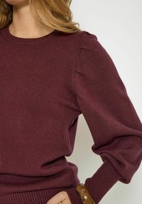 Maroon knitted sweater with a round neckline, ribbed cuffs, and balloon sleeves. Smooth texture with subtle detailing on shoulders.