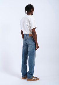 Jeans di denim azzurro chiaro con una vestibilità rilassata e un lavaggio sbiadito, abbinati a una t-shirt bianca oversize e sneaker grigie con strisce bianche.