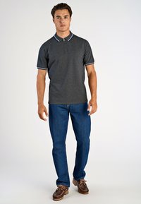 Grå pikétröja med vita och blå krageaccenter, kombinerad med blå jeans och bruna skor. Tyget verkar strukturerat och avslappnat.