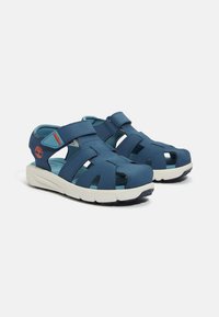 Siniset sandaalit, jotka on valmistettu sileästä synteettisestä materiaalista, joissa on leikkuut, säädettävät hihnat ja kuvioitu valkoinen kumipohja.