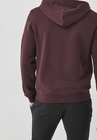 Sweat à capuche bordeaux avec une texture douce, des poignets et un ourlet côtelés, présentant une poche kangourou à l'avant et une coupe classique.