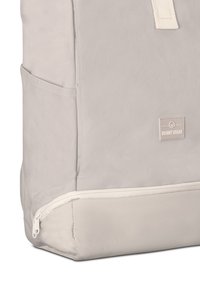 Light gray backpack made of textured fabric, featuring a zippered bottom compartment and a logo patch. Smooth accents with strong stitching.