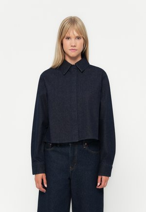 Cropped denim jacket in dark blue, featuring a spread collar, button closure, and long sleeves, with a smooth texture and minimal stitching.