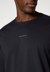 Zwart sportshirt met korte mouwen van lichtgewicht stof; heeft een ronde hals en een subtiele "SALOMON" logo op de borst.