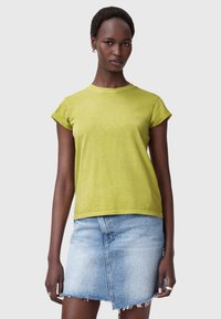 Koszulka z krótkim rękawem w limonkowym kolorze, wykonana z miękkiego materiału, z okrągłym dekoltem i luźnym krojem, w zestawieniu z dżinsową mini spódnicą.