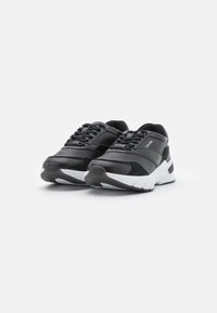 Baskets noires en cuir et daim, avec une semelle blanche coussinée, des accents texturés et une fermeture à lacets.