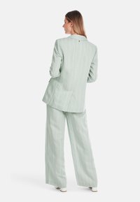 Helle grüne Blazer mit Streifen und weit geschnittene Hose. Verfügt über einen einzelnen Knopf, Revers und subtilen Textur. Taillierter Schnitt mit Schlitz hinten.