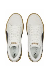 Valged sametised tossud mustade detailidega, nööbid, kuldne logo keeles ja kummine tall; sile tekstuur ja minimalism.