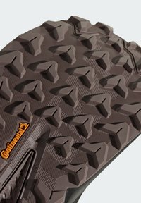 Semelle extérieure en caoutchouc brun présentant des crampons agressifs et multidirectionnels pour une meilleure traction. Surface texturée avec un logo Continental visible en orange.