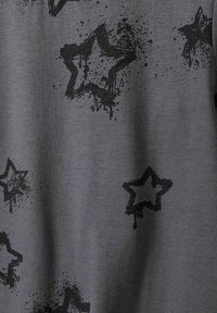 Grauer Stoff mit einer weichen Textur, der schwarze Sternformen und Spritzmuster zeigt, wodurch ein markantes Design über die Oberfläche entsteht.