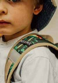 Kinder rugzak met een groen loofpatroon, grijze schouderbanden en een zwart merketiket. De rugzak heeft een gestructureerd stoffen ontwerp.