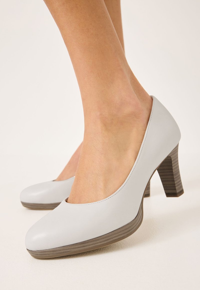 Chaussures à talons hauts en cuir gris clair avec des orteils ronds, une texture lisse et un talon en bois, présentant un design épuré et minimaliste.