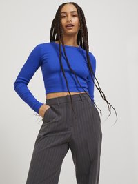 Sininen ribatulla pitkähihaisella croptopilla, jossa on pyöreä kaula-aukko, yhdistettynä harmaisiin raidoitettuihin leveälahkeisiin housuihin, joissa on sivutaskut ja rento istuvuus.