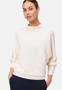 Pull crème à col haut et épaules tombantes. Doté de manches longues et d'une coupe décontractée.