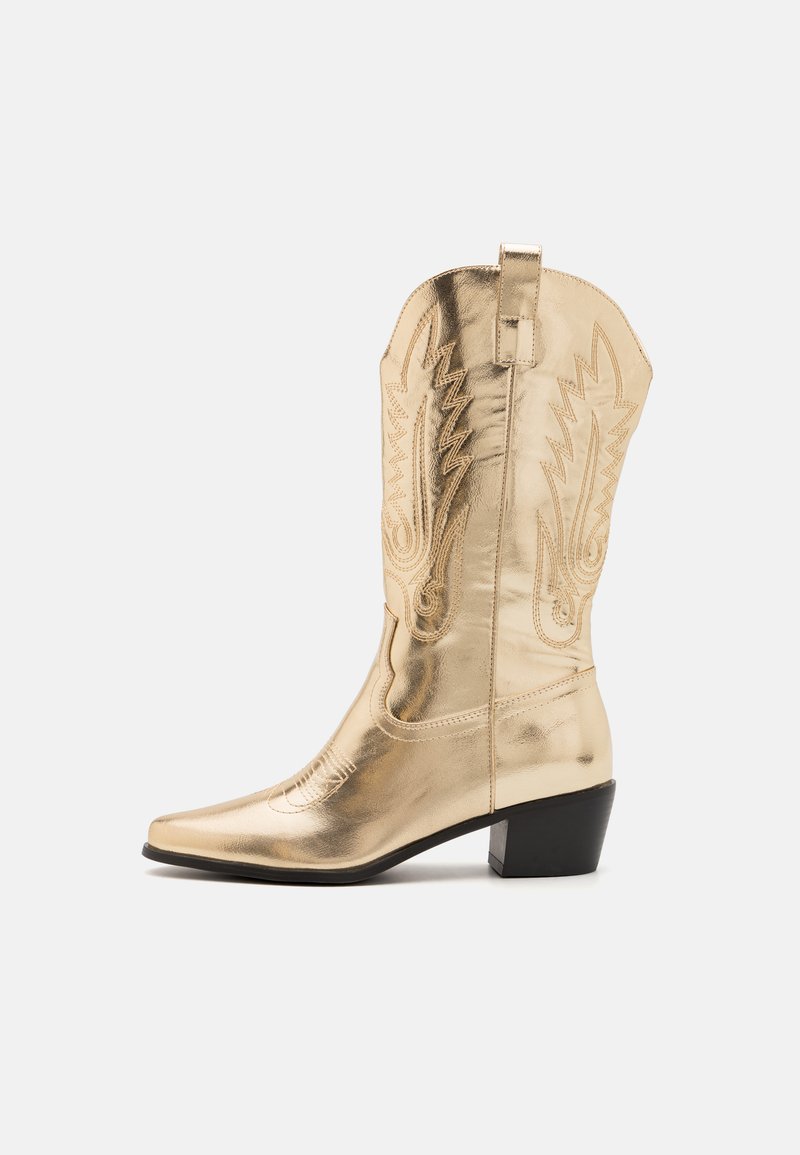 Kuldsed metallilised cowboy saapad terava varbaga, lääne stiilis õmblused ja madal, nelinurkne konts. Varustatud tõmblukuga, et neid oleks lihtne jalga panna.