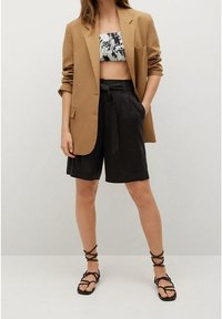 Blazer marron oversize, short noir taille haute, top bandeau à motifs. Sandales noires à lanières complètent la tenue. Design minimaliste.
