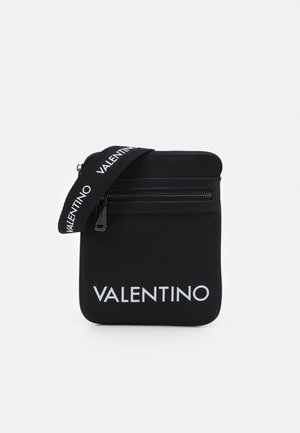 Czarna torebka Valentino na ramię z białym logo, przednia kieszeń na zamek i czarny pasek z powtarzającym się białym logo Valentino.