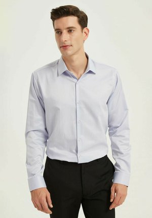 Chemise boutonnée à manches longues de couleur bleu clair, en tissu lisse, avec un col classique et un devant boutonné, assortie à un pantalon noir.